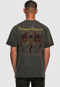 Tamsiai pilkas medvilnės marškinėliai su „Hollywood Vampires“ tekstu auksine spalva ir raudonu drakono grafiku, papildomomis atspausdintomis frazėmis bei laisvu pjūviu.