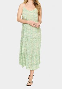 Maxi sukienka w jasnozielonym materiale z kwiatowym wzorem w żółtym i niebieskim. Posiada cienkie regulowane ramiączka oraz zwiewny, warstwowy krój.