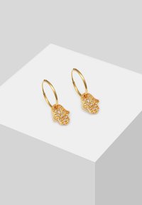 Des boucles d'oreilles en or en forme de créoles présentent un charm en forme de main orné de cristaux transparents. Le design met l'accent sur des détails raffinés et une finition polie.