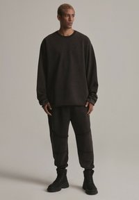 Ciemny, oversize'owy dres i zwężane spodnie dresowe z fakturowanej tkaniny. Na spodniach znajdują się wszyte akcenty. W połączeniu z czarnymi butami.