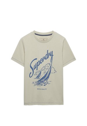 Maglietta beige a maniche corte con illustrazioni di barche a vela blu, la parola "Superdry" in grande scrittura e il testo "Hand of Quality" sotto.