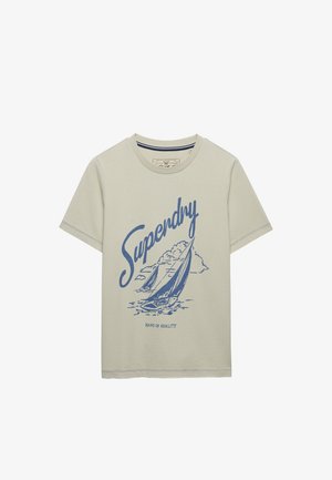 T-shirt beige à manches courtes avec illustrations de voiliers bleus, le mot "Superdry" en grande écriture stylisée, et le texte "Hand of Quality" en dessous.