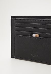 Black wallet made of textured material with multiple card slots, a visible card in one pocket, and embossed brand logo on the front.