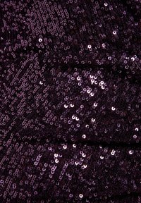 Gros plan de paillettes violet foncé scintillantes, densément agencées sur un tissu, reflétant la lumière avec des rangées courbes et une surface texturée.