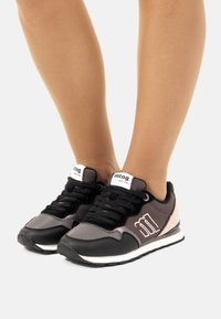 Schwarze und graue Sport-Sneaker mit einem pinken Akzent, Obermaterial aus Textil und Synthetik, Schnürverschluss und einer weißen Zwischensohle.
