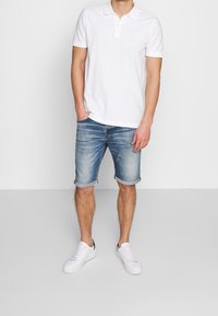 Bílá polo triko s límečkem a krátkými rukávy, spojené se světle modrými denimovými šortkami s ohrnutým lemem a bílými teniskami.