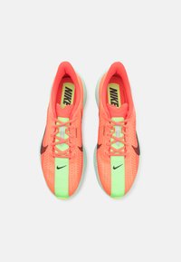 Baskets de course Nike avec une tige en mesh de couleur orange néon vif, accentuées par une bande verte et un swoosh noir, avec des lacets plats.