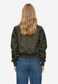 Olivově zelená bomber bunda s nadýchanými rukávy, žebrovaným lemem a manžetami, kombinovaná s modrými džíny, pohled zezadu.