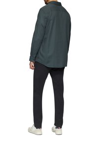 Dunkelgrünes Langarmhemd mit einem Button-Down-Kragen, strukturiertem Stoff und schwarzen Hosen, kombiniert mit weißen Sneakers mit marineblauen und roten Akzenten.