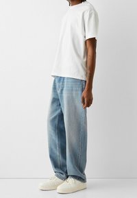 Bílé tričko z bavlny s krátkými rukávy ve spojení s světle modrými, volně střiženými džínami. Obuv tvoří bíl é nízké tenisky.