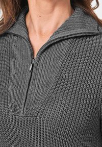 Grijze gebreide pullover met een halve rits bij de kraag, voorzien van een geribbelde textuur en een decoratief patroon op de borst.