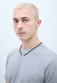 Must mustreket juhe, millel on hõbedane aktsent, kantud halli t-särgi üle. Modellil on lühikesed blondid juuksed ja sinised silmad, heledal taustal.