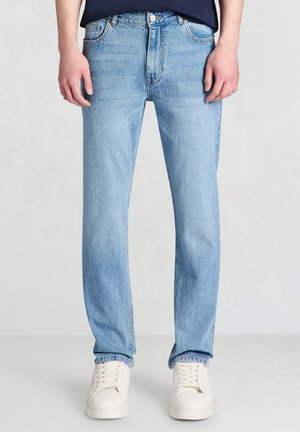 Jeans in denim azzurro chiaro con taglio dritto, cinque tasche e scoloritura minima; abbinati a sneakers bianche.