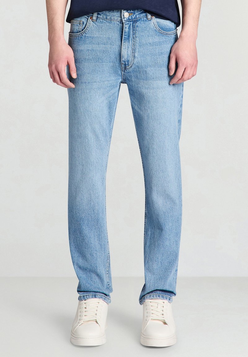 Jeans in denim azzurro chiaro con taglio dritto, cinque tasche e scoloritura minima; abbinati a sneakers bianche.