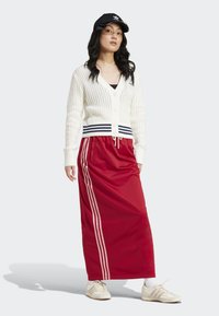 Cardigan de malha branca com riscas azuis, combinado com uma saia longa vermelha com riscas brancas nas laterais. Ténis brancos completam o visual.