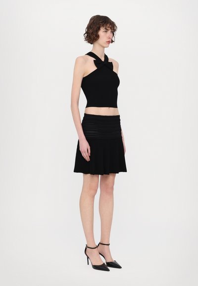 Melnā halter top ar loku, apvienojot ar melnu plisētu mini svārku. Modelis nēsā melnas augstpapēžu kurpes ar potītes siksnām.