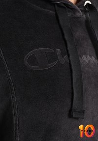 Sudadera con capucha negra hecha de tela suave. Presenta un logo tonal en el pecho y cordones de contraste. Diseño minimalista sin patrones adicionales.
