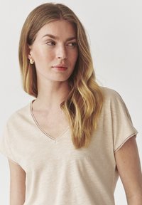 Light beige V-neck t-shirt made of soft fabric, featuring short sleeves and subtle stitching details along the neckline and sleeves.
