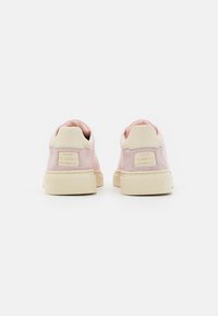 Blassrosa Sneaker mit glattem Obermaterial, kontrastierender cremefarbener Gummisohle und Markenakzenten an der Ferse. Texturierte Oberfläche für besseren Halt.