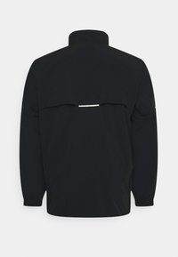 Veste noire à manches longues avec col montant et rabat de ventilation à l'arrière comportant une petite bande réfléchissante horizontale.