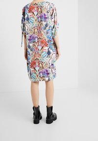 Bunt gemustertes Kleid mit kurzen Ärmeln und lockerem Schnitt, aus leichtem Stoff, getragen mit schwarzen Knöchelstiefeln.