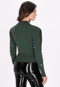 Groene gebreide trui met een aansluitend ontwerp, ronde hals en geribbelde zoom. Bevat knopen met een glanzende afwerking langs de mouwen.