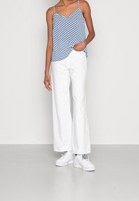 Randig blå och vit linne med tunna axelband, tillsammans med vita vida byxor och vita platåskor med färgglada accenter.