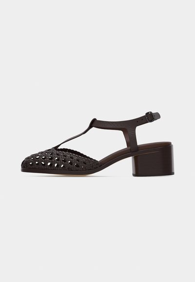 Sandale T-strap en cuir tressé marron foncé avec talon bloc et fermeture à boucle à la cheville, présentant un design élégant et respirant.