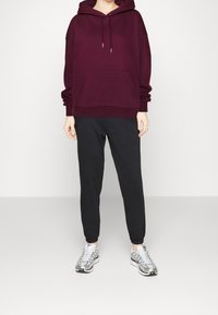 Sudadera de gran tamaño color marrón oscuro con bolsillo frontal, combinada con pantalones negros ajustados y zapatillas plateadas con un diseño estampado.