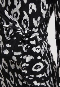 Svart och vit leopardmönstrad tyg med en knuten rosett, som visar upp en texturerad design och en flödande silhuett.