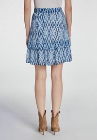 Jupe tiered à motif bleu avec un ourlet volanté et une taille élastique. Le matériau semble léger et semi-transparent. Accompagnée de bottes à talons marron.