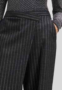 Zwarte pinstriped broek met een op maat gemaakte design, voorzien van een platte tailleband en subtiele glans, die de textuur van de stof benadrukt.