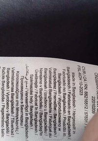 Care label in white fabric with black text. Information includes "Made in Bangladesh" and translations in multiple languages.