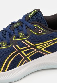 Scarpa da corsa navy con tessuto in mesh, dettagli neri e accenti neon verde e rosa. Presenta una suola testurizzata per aderenza e supporto.