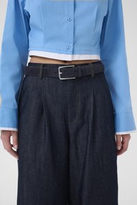 Avkortet blå skjorte med knapper, kombinert med mørke denim-bukser, med belte med sølvspenne og gule sømmer på lommene.