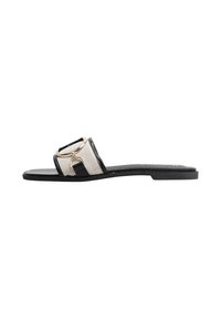 Sandalia plana negra con una amplia correa de malla y un acento circular dorado. Diseño simple con un acabado suave y una suela minimalista.