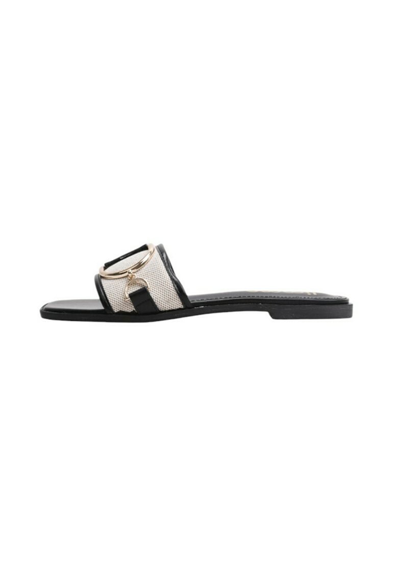 Sandalia plana negra con una amplia correa de malla y un acento circular dorado. Diseño simple con un acabado suave y una suela minimalista.