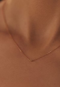 Delicate gouden ketting met een fijn, gekoppeld ontwerp, rustend op een glad, gebruind huidoppervlak, wat de slanke vorm en subtiele glans benadrukt.