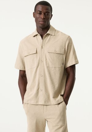 Kurzärmeliges, beige Hemd mit Knopfleiste aus strukturiertem Stoff, zwei Taschen vorne und klassischem Kragen, kombiniert mit passenden Hosen.