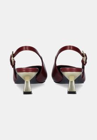 Tacones slingback de cuero burdeos con puntera redondeada, tacón cuadrado con acentos metálicos y correa ajustable en el tobillo. Textura suave, diseño minimalista.
