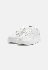 Sneakers bianchi con dettagli perforati, lacci piatti e suole bianche spesse. Presentano un sottile logo del brand sulla linguetta e un accento testurizzato sul tallone.