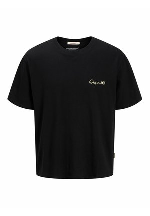 Băiat stând, purtând tricou negru, pantaloni scurți din denim bleu deschis, șosete albe și adidași alb-negru pe fundal alb simplu.