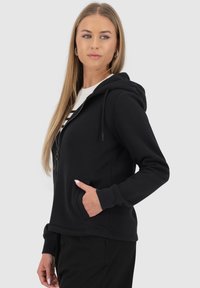 Felpa nera con zip, dotata di tasca frontale, cappuccio con cordino e polsini a costine. Il tessuto sembra liscio e leggermente elastico.