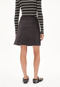 Koolstofkleurige corduroy A-lijn rok met achterzakken, gedragen met een zwart-wit gestreepte blouse met lange mouwen en zwarte schoenen met zilveren accenten.