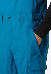 Blauw waterdichte overall met een gladde textuur, voorzien van zijzakken, verstelbare schouderbanden en een klein "DRYVENT" logo op de borst.