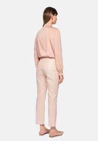 Blushrosa Bluse mit langen Ärmeln und weicher Textur, kombiniert mit hellrosa, maßgeschneiderten Hosen. Glatte, elegante Oberfläche mit minimalen Details.