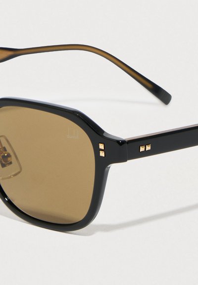 Fekete műanyag napszemüveg barna lencsékkel, arany díszítéssel a szárakon. Téglalap alakú, elegáns kialakítású, sima felületű.