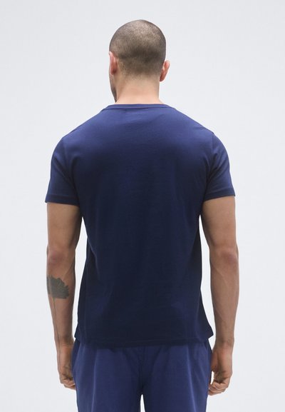 Tmavomodré tričko s krátkym rukávom z mäkkej tkaniny, so zvieracím okrúhlym výstrihom a hladkou textúrou, nosené spolu s rovnakými nohavicami.