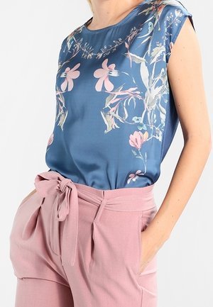 Top in satin blu con motivo floreale e maniche a cappuccio, abbinato a pantaloni rosa chiaro a vita alta con dettaglio del nodo in vita.