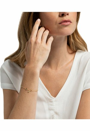 Goldarmband mit mehreren dekorativen Anhängern, die eine Mischung aus runden und ovalen Formen aufweisen, vor einem hellen Hintergrund und am Handgelenk getragen.
